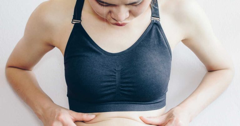 Woman touching her fat belly, woman's hand holding excessive belly fat.