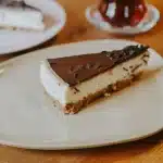 Golden-brown apple crisp cheesecake bar with layers of crust, cheesecake, apples, and oat topping