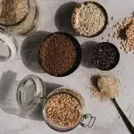 Assortment of whole grains, legumes, fresh vegetables and herbs on a wooden table with olive oil