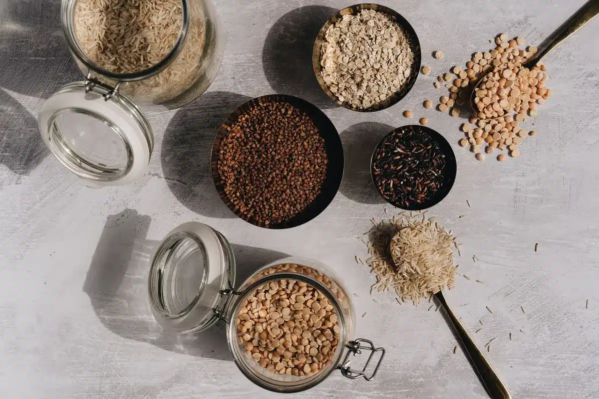 Assortment of whole grains, legumes, fresh vegetables and herbs on a wooden table with olive oil