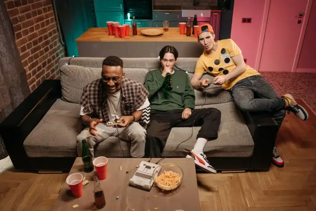 Person sitting on couch in dim room illuminated by TV screen, surrounded by snacks, late at night