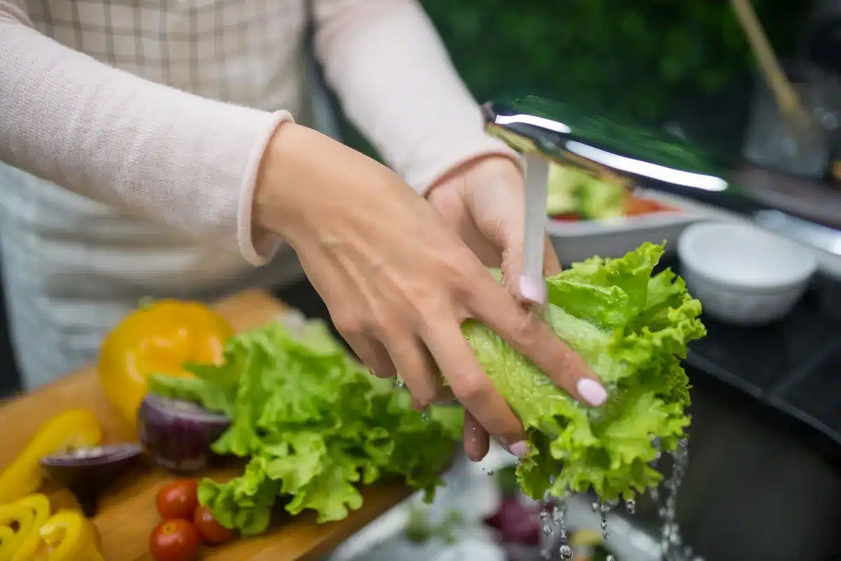 Hands rinsing fresh vegetables under running water in a kitchen sink