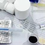 Medicamentos para el colesterol, jeringas y equipo de monitoreo clínico sobre una superficie de laboratorio.