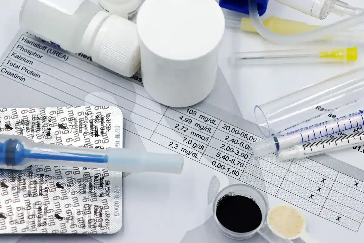 Medicamentos para el colesterol, jeringas y equipo de monitoreo clínico sobre una superficie de laboratorio.