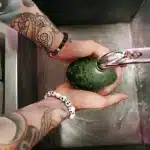 Hands rinsing fresh vegetables and fruits under running water in a kitchen sink