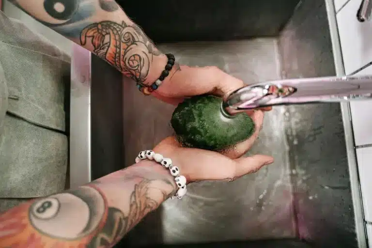 Hands rinsing fresh vegetables and fruits under running water in a kitchen sink