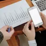 Person's hands holding a smartphone displaying a form on a desk with papers and tea nearby