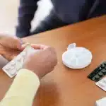 A hand holding a single pill over a weekly calendar, symbolizing simplified once-weekly HIV treatment