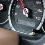 Close-up of hands on steering wheel with dashboard mileage counter visible