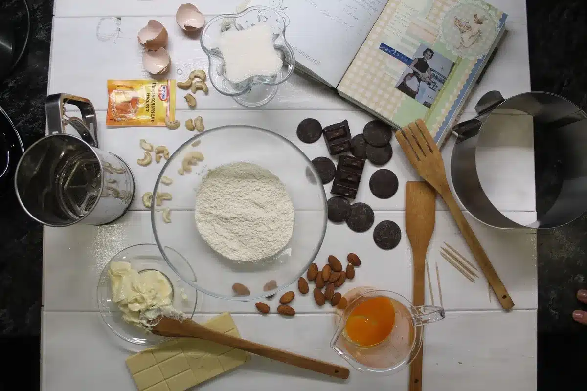 Baking ingredients laid out on a countertop: butter, chocolate, eggs, cream cheese, and other pantry staples