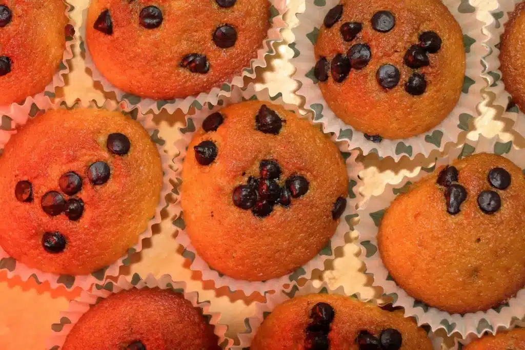Golden strawberry muffins in a muffin tin with fresh berries and powdered sugar nearby
