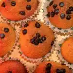 Golden strawberry muffins in a muffin tin with fresh berries and powdered sugar nearby