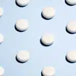 Blister pack of pain relief tablets next to a glass of water on a medical desk