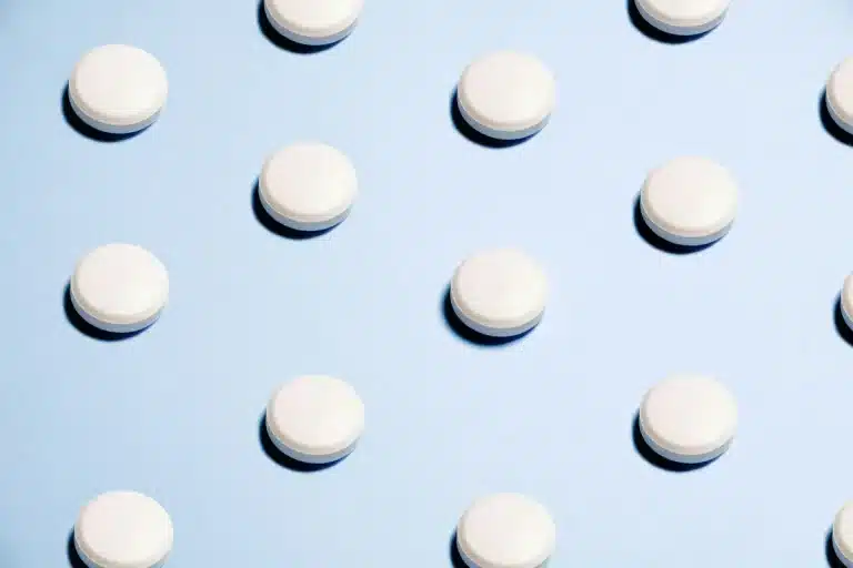 Blister pack of pain relief tablets next to a glass of water on a medical desk