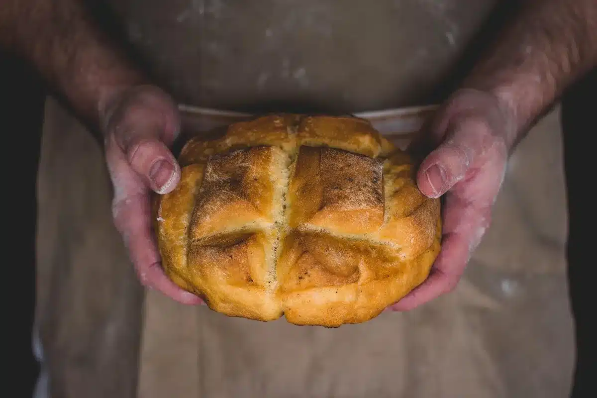 Hands pressing graham cracker crust mixture firmly into a parchment-lined baking pan