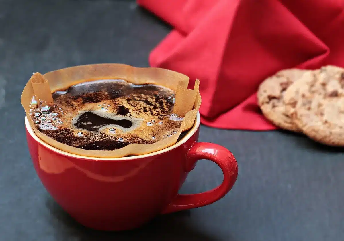 Hands pouring freshly brewed coffee into a white cup from a filter coffee maker