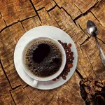 Daylit kitchen table with a hot cup, hand and thermometer to check temperature