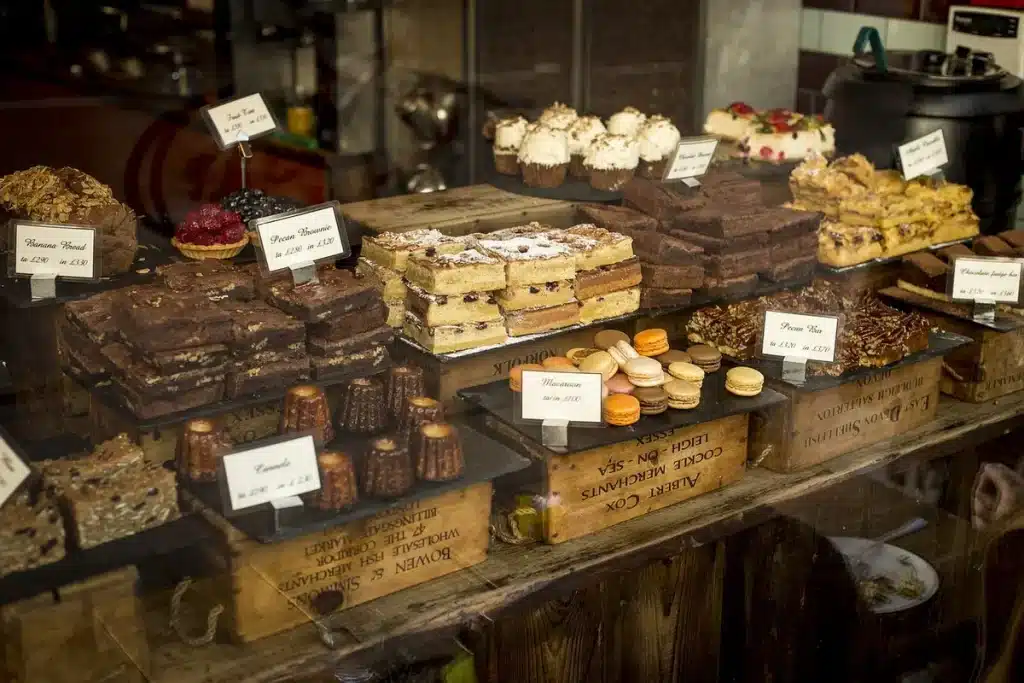 Manos colocando tartas frescas y frutas tropicales en un mostrador de panaderÃa artesanal iluminado por la mañana