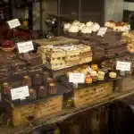Manos colocando tartas frescas y frutas tropicales en un mostrador de panadería artesanal iluminado por la mañana