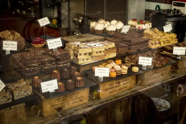 Manos colocando tartas frescas y frutas tropicales en un mostrador de panadería artesanal iluminado por la mañana