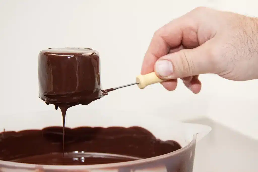 Tray of red velvet cake balls being dipped in white chocolate coating