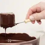 Tray of red velvet cake balls being dipped in white chocolate coating
