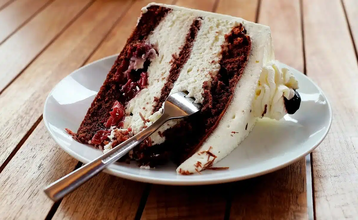 Cream cheese frosting being spread over a cooled cake with a spatula