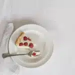 Summer berry sheet cake topped with cream cheese frosting and fresh raspberries and blueberries on a white plate