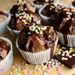 Muffin tin of Oreo cheesecake cupcakes with glossy ganache being spooned on in daylight