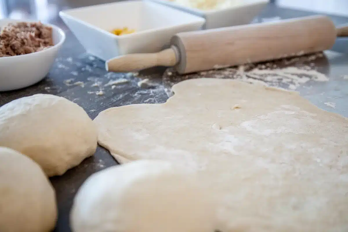 Spreading tomato sauce over a precooked pinsa on an oven tray