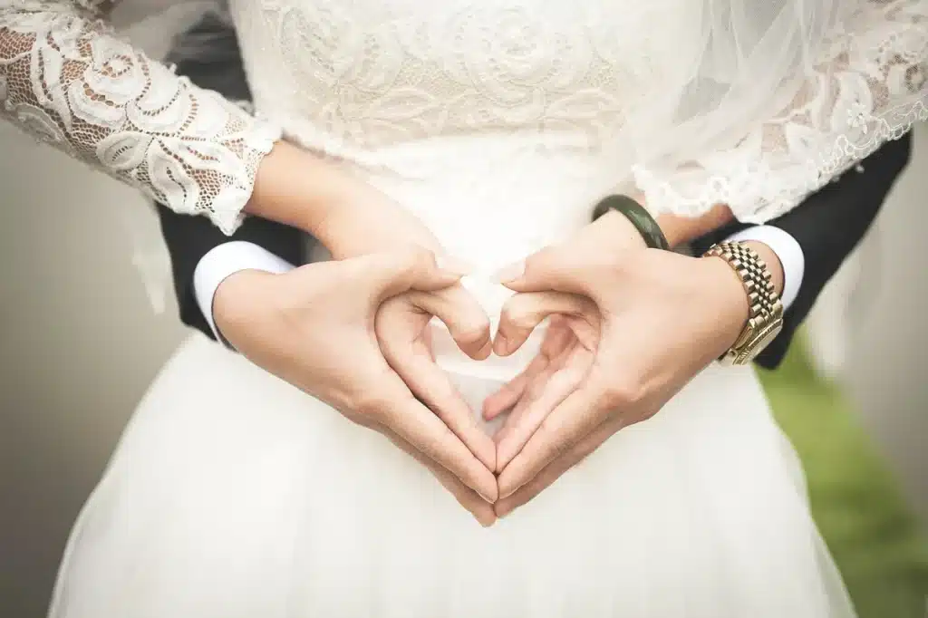 Main lumineuse d'une personne arrangeant un boutonnière près d'une invitation de mariage sur une table de jardin