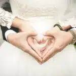 Main lumineuse d'une personne arrangeant un boutonnière près d'une invitation de mariage sur une table de jardin